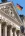 Fragment fasady budynku Reichstagu w Berlinie z kolumnami i rzeźbionym frontonem z napisem „Dem Deutschen Volke”, nad którym powiewa niemiecka flaga na tle błękitnego nieba.
